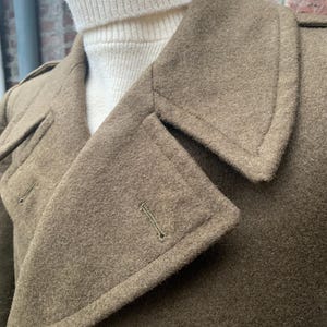 May include: A brown wool coat with a large collar and a button closure. The coat has a textured surface and a single button on the front.