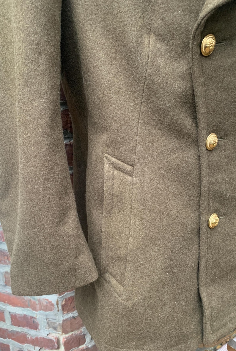 May include: A brown wool peacoat with a double breasted closure and gold buttons. The coat has a flap pocket on the right side.