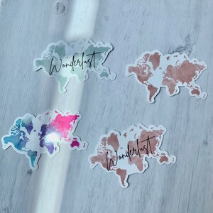 May include: Four world map stickers with the word "Wanderlust" written on them. The maps are in different colors: blue, pink, green, and brown.