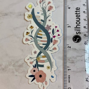 May include: A sticker featuring a stylised DNA double helix intertwined with floral elements. The DNA is depicted in shades of blue, grey, and yellow, with pink, white, and yellow flowers surrounding it. The sticker is approximately 5 cm tall.
