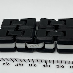 May include: A black and white fidget toy with the word "ANY" printed on one of the white links. The toy is made of interlocking black and white blocks. A ruler is in the foreground, showing measurements in millimetres.