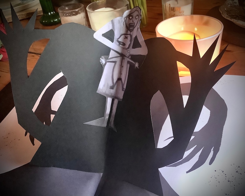 May include: A black paper cutout of a monster with long arms and sharp claws. The monster is holding a white paper cutout of a woman with a child in her arms. The woman is looking up in fear.