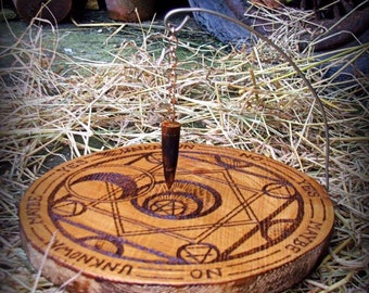 May include: A wooden divination board with etched symbols and the words "Unknown", "Maybe", "Yes", and "No". A pendulum hangs above the board. The board is on a bed of straw.