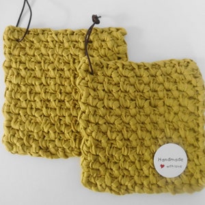 Könnte beinhalten: Zwei gelbe Topflappen aus Häkelarbeit mit braunen Lederschlaufen. Ein weißes Etikett mit dem Text "Handmade with love" ist an einem der Topflappen befestigt.