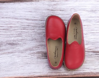May include: A pair of red leather slip-on shoes with a pointed toe and a small, decorative detail on the top. The shoes have a brown leather sole and the brand name "Solecraft Handmade" is printed on the inside of each shoe.