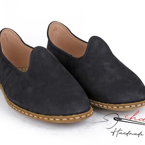 Puede incluir: Un par de zapatos negros de cuero sin cordones con un ribete cosido marr&oacute;n alrededor de la suela. Los zapatos son hechos a mano y tienen un aspecto casual y c&oacute;modo.