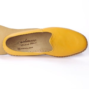 May include: A pair of yellow leather slip-on shoes with a brown leather sole. The shoes have a simple design and are made of high-quality leather. The brand name "charoqf" is printed on the inside of the shoe.