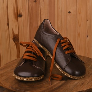 May include: A pair of brown leather lace-up shoes with orange laces. The shoes are sitting on a wooden table.