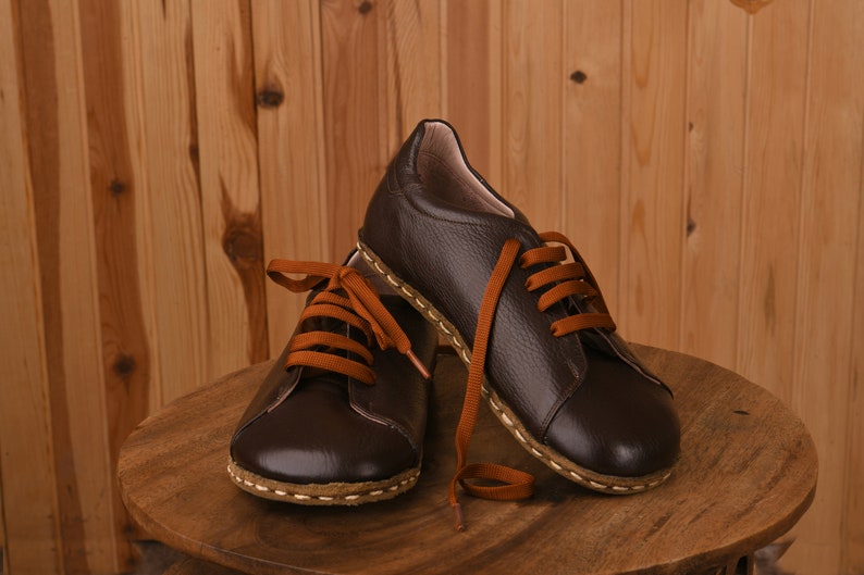 May include: A pair of brown leather lace-up shoes with orange laces. The shoes are sitting on a wooden table.