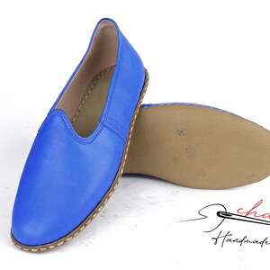 Pu&ograve; includere: Un paio di scarpe blu in pelle da indossare senza lacci con suola in pelle marrone. Le scarpe hanno una punta a punta e un design semplice. Il nome del marchio "charoog Handmade Footwear" &egrave; visibile nell'angolo in basso a destra dell'immagine.