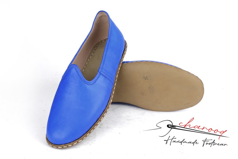 Pu&ograve; includere: Un paio di scarpe blu in pelle da indossare senza lacci con suola in pelle marrone. Le scarpe hanno una punta a punta e un design semplice. Il nome del marchio "charoog Handmade Footwear" &egrave; visibile nell'angolo in basso a destra dell'immagine.