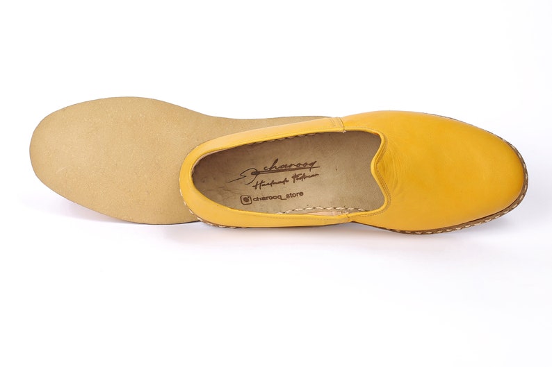 May include: A pair of yellow leather slip-on shoes with a brown leather sole. The shoes have a simple design and are made of high-quality leather. The brand name "charoqf" is printed on the inside of the shoe.