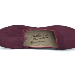 May include: Burgundy suede leather slip-on shoes with a brown leather insole. The insole has the text "Charooq Handmade Footwear" and "@charooq_store".