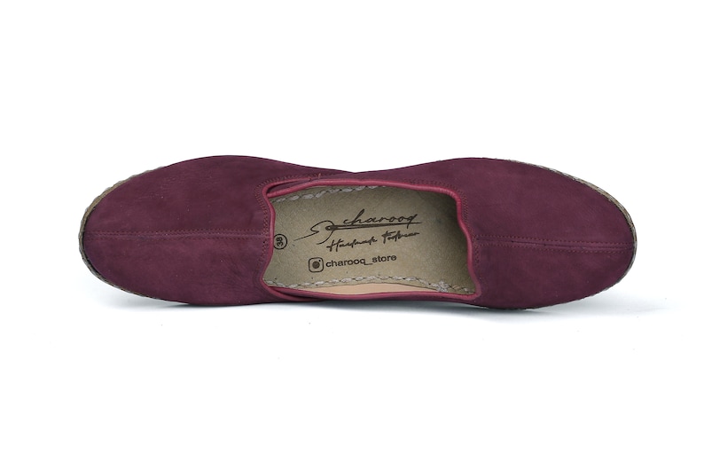 May include: Burgundy suede leather slip-on shoes with a brown leather insole. The insole has the text "Charooq Handmade Footwear" and "@charooq_store".