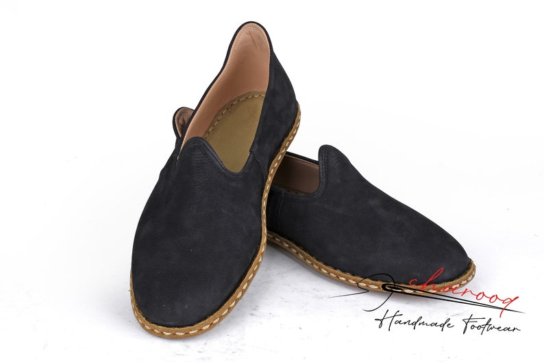 Puede incluir: Un par de mocasines de ante negro con ribete de cuero marr&oacute;n. Los mocasines tienen un dise&ntilde;o sencillo y son perfectos para el uso casual.