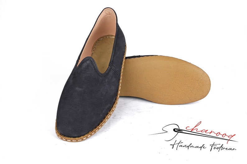 Puede incluir: Un par de zapatos negros de cuero con deslizamiento con una suela de cuero marr&oacute;n y un borde cosido. Los zapatos son hechos a mano y tienen un aspecto casual y c&oacute;modo.