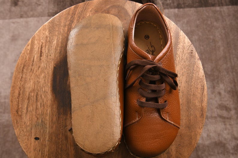 May include: A pair of brown leather lace-up shoes with a brown leather sole. The shoes are on a wooden surface.
