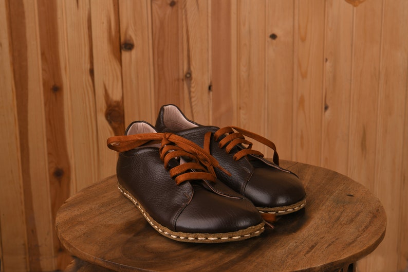 May include: A pair of brown leather lace-up shoes with orange laces. The shoes are sitting on a wooden surface.