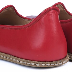 Puede incluir: Un par de zapatillas de cuero rojo. Las zapatillas tienen una puntera redondeada y un perfil bajo. Las suelas son de color marr&oacute;n claro con costuras visibles alrededor de los bordes. Las zapatillas est&aacute;n dise&ntilde;adas para uso en interiores y son de cuero suave.