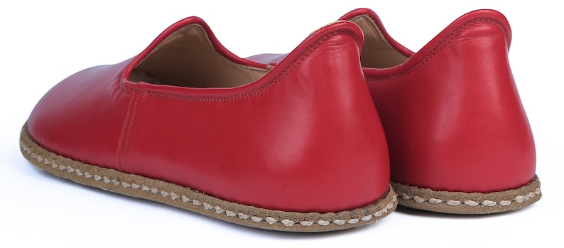 Puede incluir: Un par de zapatillas de cuero rojo. Las zapatillas tienen una puntera redondeada y un perfil bajo. Las suelas son de color marr&oacute;n claro con costuras visibles alrededor de los bordes. Las zapatillas est&aacute;n dise&ntilde;adas para uso en interiores y son de cuero suave.