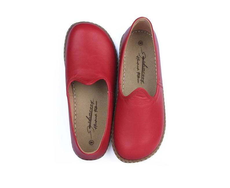 Puede incluir: Un par de zapatos rojos de cuero sin cordones. Los zapatos tienen una puntera redondeada y una suela cosida. El interior del zapato tiene un logotipo impreso y el n&uacute;mero 40. Los zapatos se muestran sobre un fondo blanco.