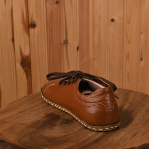 May include: A brown leather shoe with laces. The shoe is sitting on a wooden surface.