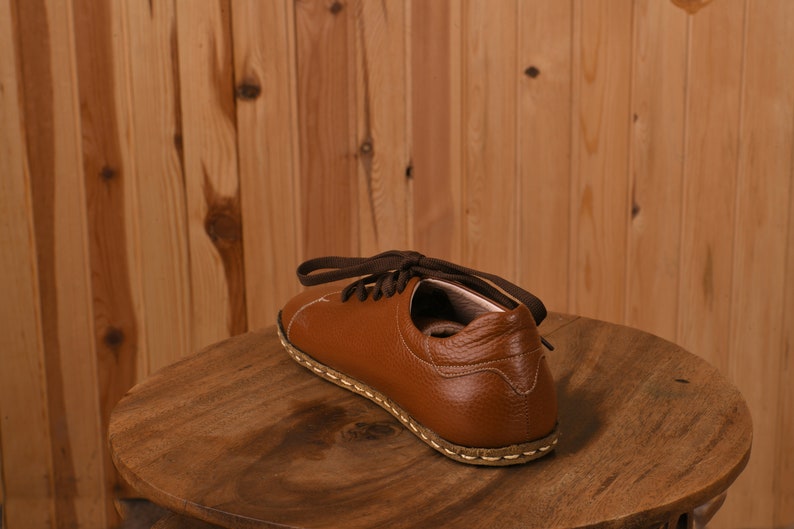 May include: A brown leather shoe with laces. The shoe is sitting on a wooden surface.