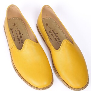 May include: A pair of yellow leather slip-on shoes with a stitched edge. The shoes have a simple design and are made of soft leather.