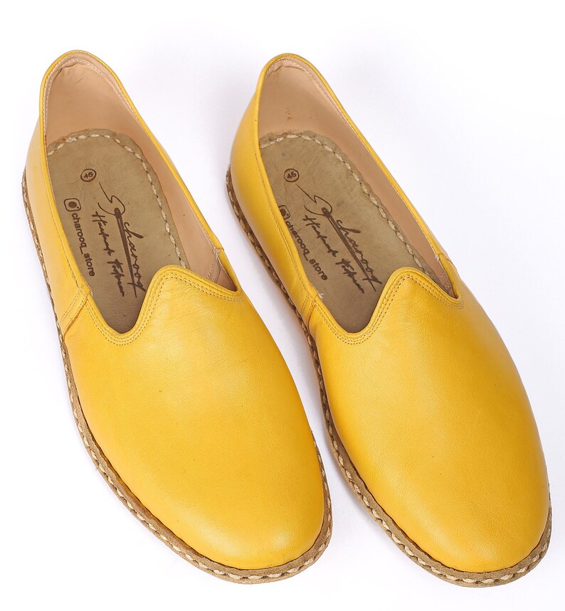May include: A pair of yellow leather slip-on shoes with a stitched edge. The shoes have a simple design and are made of soft leather.