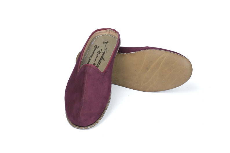 May include: A pair of burgundy suede slippers with a woven jute sole. The slippers have a simple design and are perfect for casual wear.
