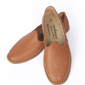 May include: A pair of brown leather slip-on shoes with a stitched edge. The shoes have a pointed toe and a flat sole. The brand name "Charcoal" is printed on the inside of the shoe.