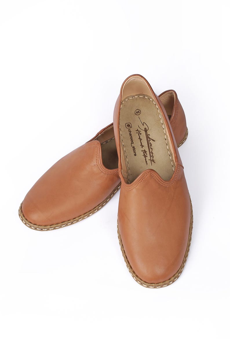 May include: A pair of brown leather slip-on shoes with a stitched edge. The shoes have a pointed toe and a flat sole. The brand name "Charcoal" is printed on the inside of the shoe.