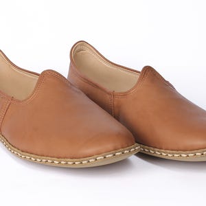 May include: A pair of brown leather slip-on shoes with a stitched edge.