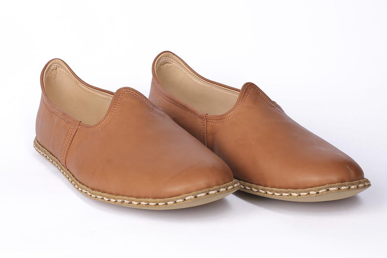 May include: A pair of brown leather slip-on shoes with a stitched edge.