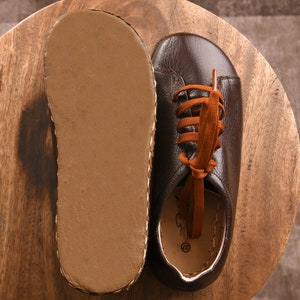 May include: A pair of brown leather shoes with orange laces. The shoes are on a wooden surface and the soles are visible.