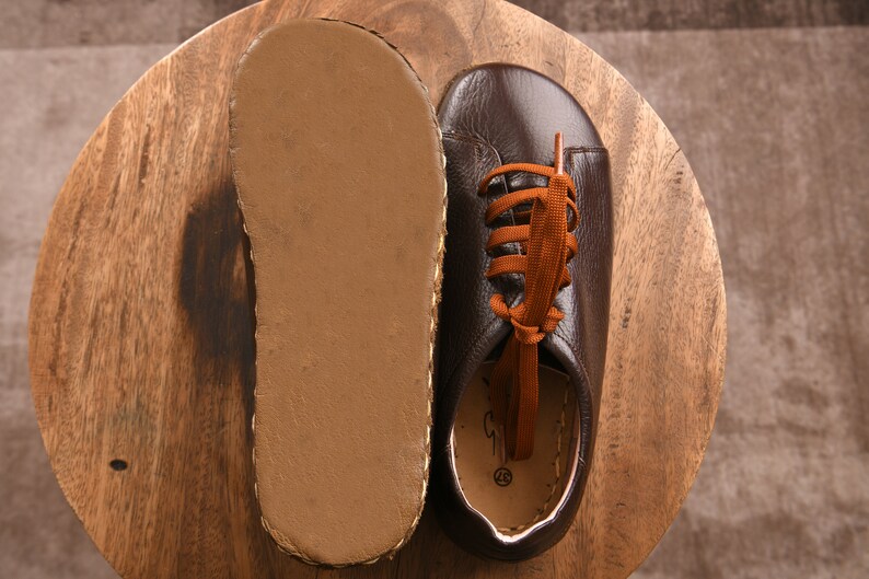 May include: A pair of brown leather shoes with orange laces. The shoes are on a wooden surface and the soles are visible.