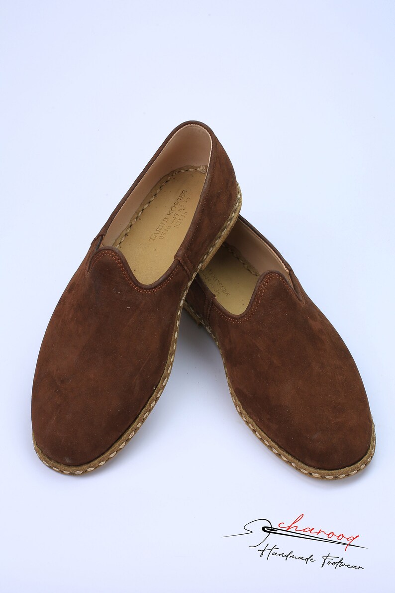May include: A pair of brown suede slip-on shoes featuring a rounded toe, a tan interior lining, and visible light-colored stitching along the sole edge. The interior sole is stamped with the text TARIK KOSGER 0536 445 03 38 KU 13.