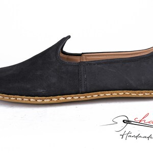 Puede incluir: Zapatos negros de cuero con cierre de slip-on y suela cosida marr&oacute;n. Los zapatos tienen una punta puntiaguda y una parte superior ligeramente curvada.