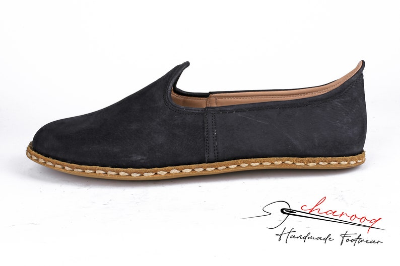 Puede incluir: Zapatos negros de cuero con cierre de slip-on y suela cosida marr&oacute;n. Los zapatos tienen una punta puntiaguda y una parte superior ligeramente curvada.