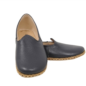 May include: A pair of dark blue leather slip-on shoes with a brown stitched trim around the sole.
