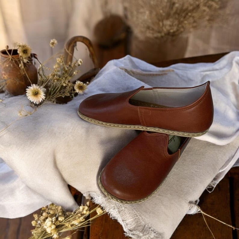 May include: A pair of brown leather slip-on shoes with a simple design. The shoes are made of soft leather and have a comfortable fit.