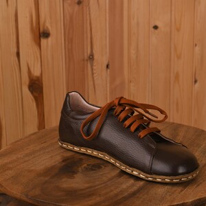 May include: A brown leather shoe with orange laces on a wooden surface.