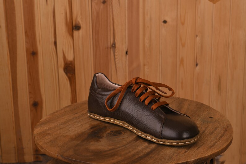 May include: A brown leather shoe with orange laces on a wooden surface.