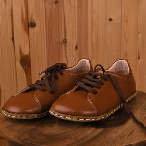 May include: Two brown leather lace-up shoes with white stitching on a wooden surface.