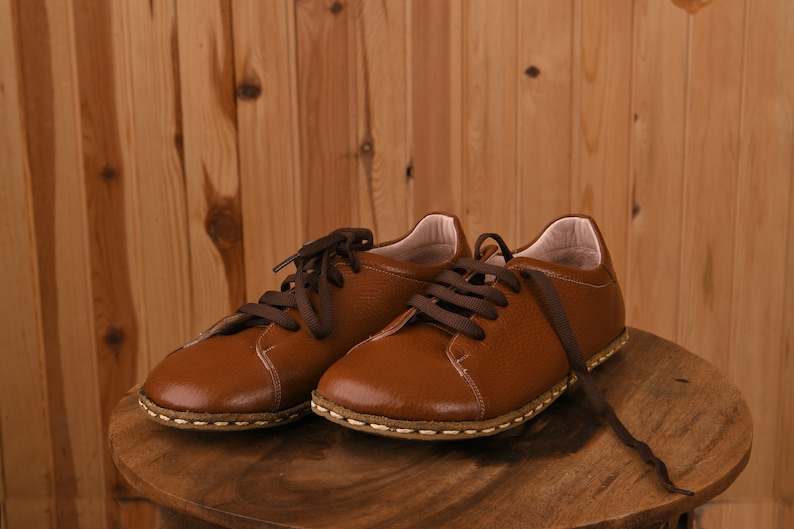 May include: Two brown leather lace-up shoes with white stitching on a wooden surface.