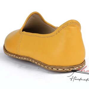 May include: A pair of yellow leather slip-on shoes with a stitched edge and a brown leather sole.