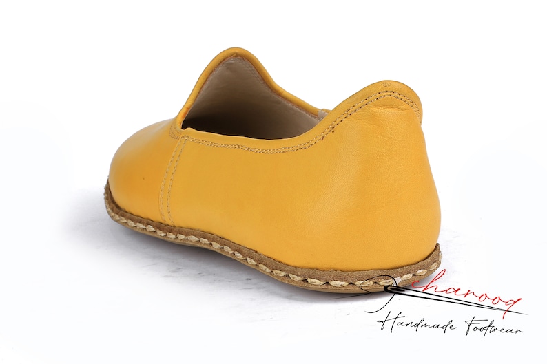 May include: A pair of yellow leather slip-on shoes with a stitched edge and a brown leather sole.