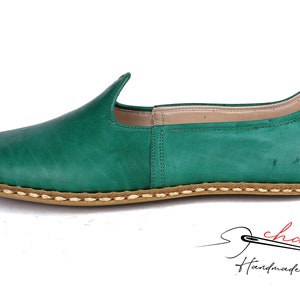 May include: Green leather slip-on shoes with a stitched brown sole. The shoes have a pointed toe and a slightly curved back.