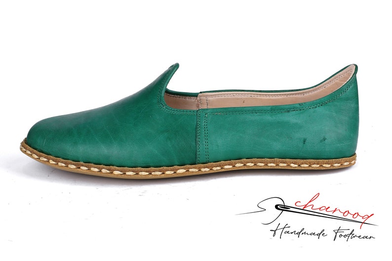 May include: Green leather slip-on shoes with a stitched brown sole. The shoes have a pointed toe and a slightly curved back.