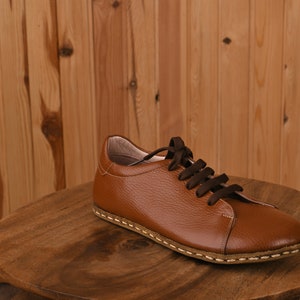 May include: A brown leather lace-up shoe with a stitched sole. The shoe is sitting on a wooden surface.